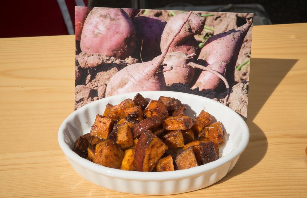 A bowl of roasted sweet potato cubes in front of a photo of whole sweet potatoes