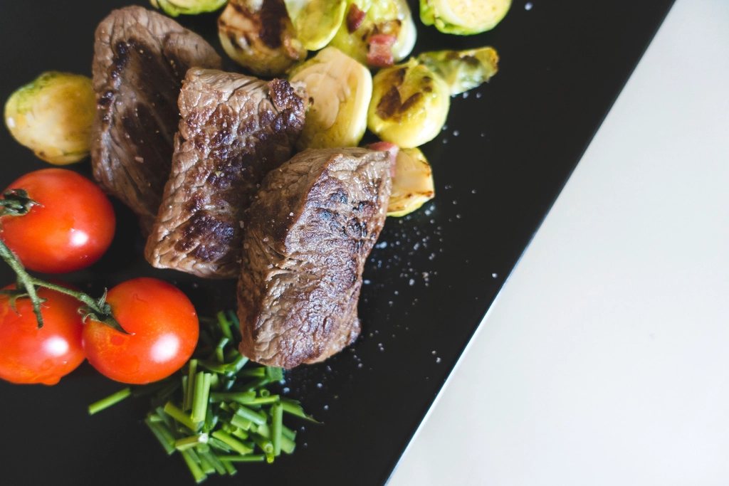 Seared beef steak pieces with grilled Brussels sprouts, vine tomatoes and chives on a black slate