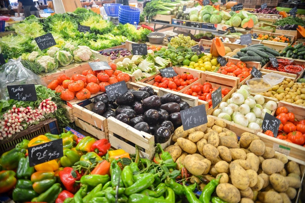 A market stall packed with crates of fresh vegetables: peppers, tomatoes, aubergines, potatoes, onions and greens